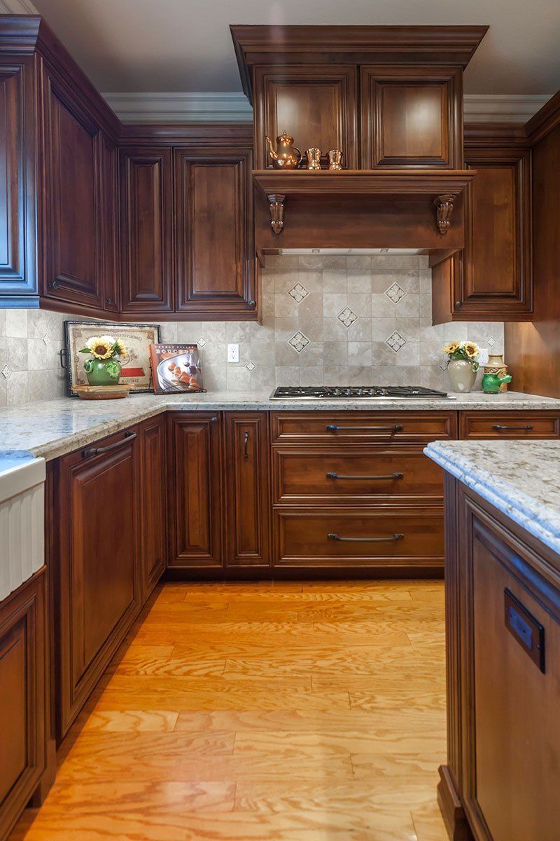 Warm-toned kitchen with dark wood cabinets, light stone countertops, and a tiled backsplash