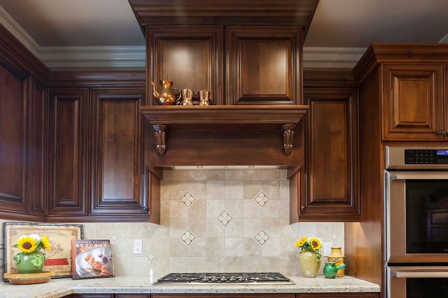 Dark wood kitchen cabinets framing a stovetop and stone backsplash with decorative items on the counters