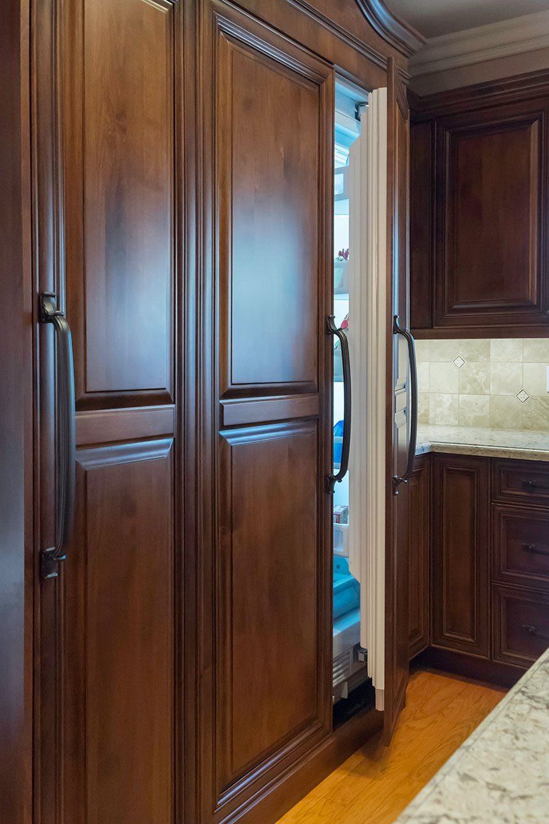 Tall dark-wood pantry doors cracked open in a kitchen, showing a narrow gap of stored items.