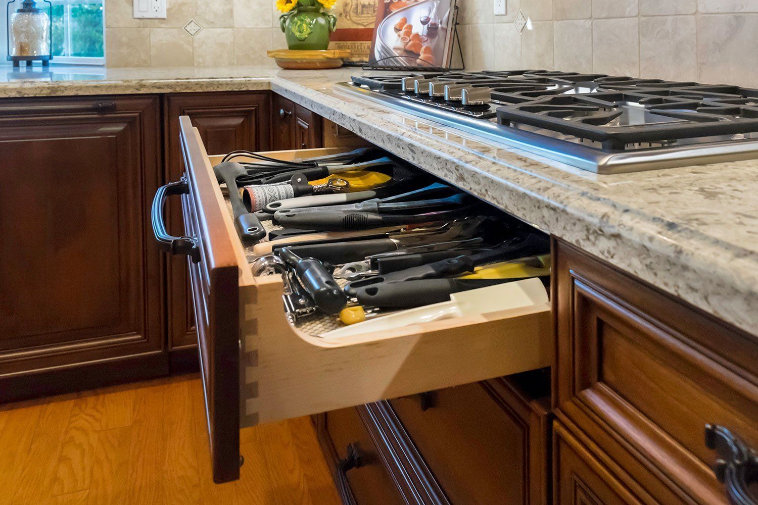 Kitchen drawer filled with cutlery and utensils pulled open beneath a granite countertop