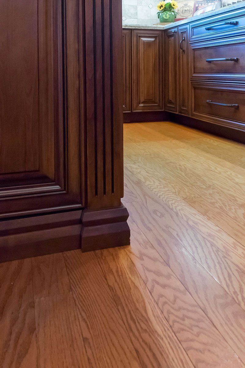 Wooden kitchen cabinets and hardwood floor with a narrow walkway and flowers on the counter