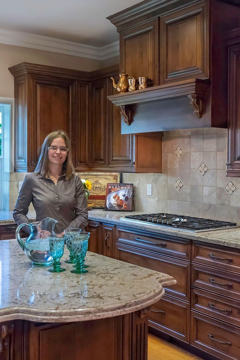 Woman standing in a warm-toned kitchen beside a granite island and wooden cabinets