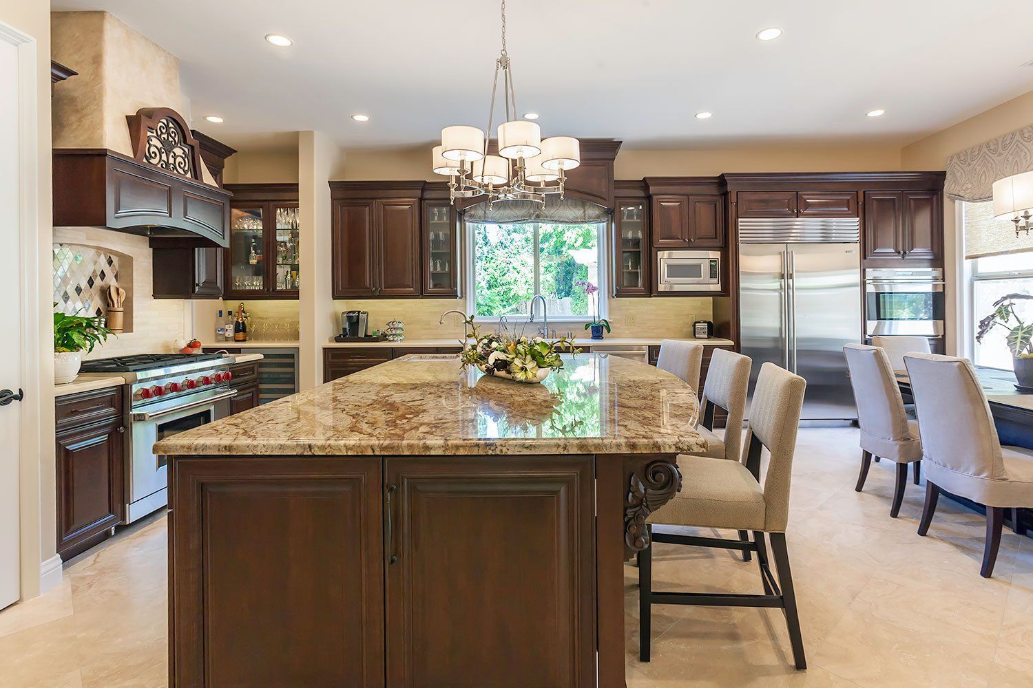 Spacious kitchen with dark wood cabinets, granite island, chandelier, and stainless steel refrigerator