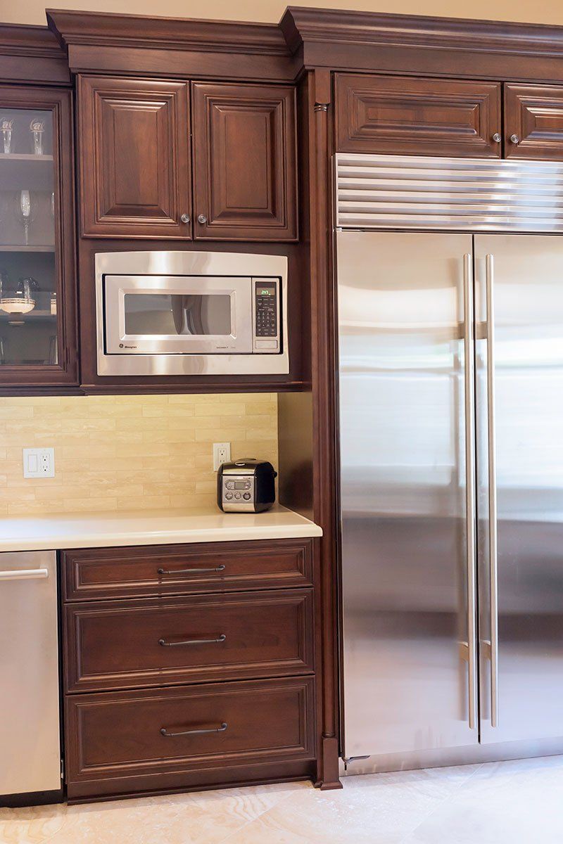 Kitchen with dark wood cabinets, stainless steel microwave and double-door refrigerator, and light countertop.
