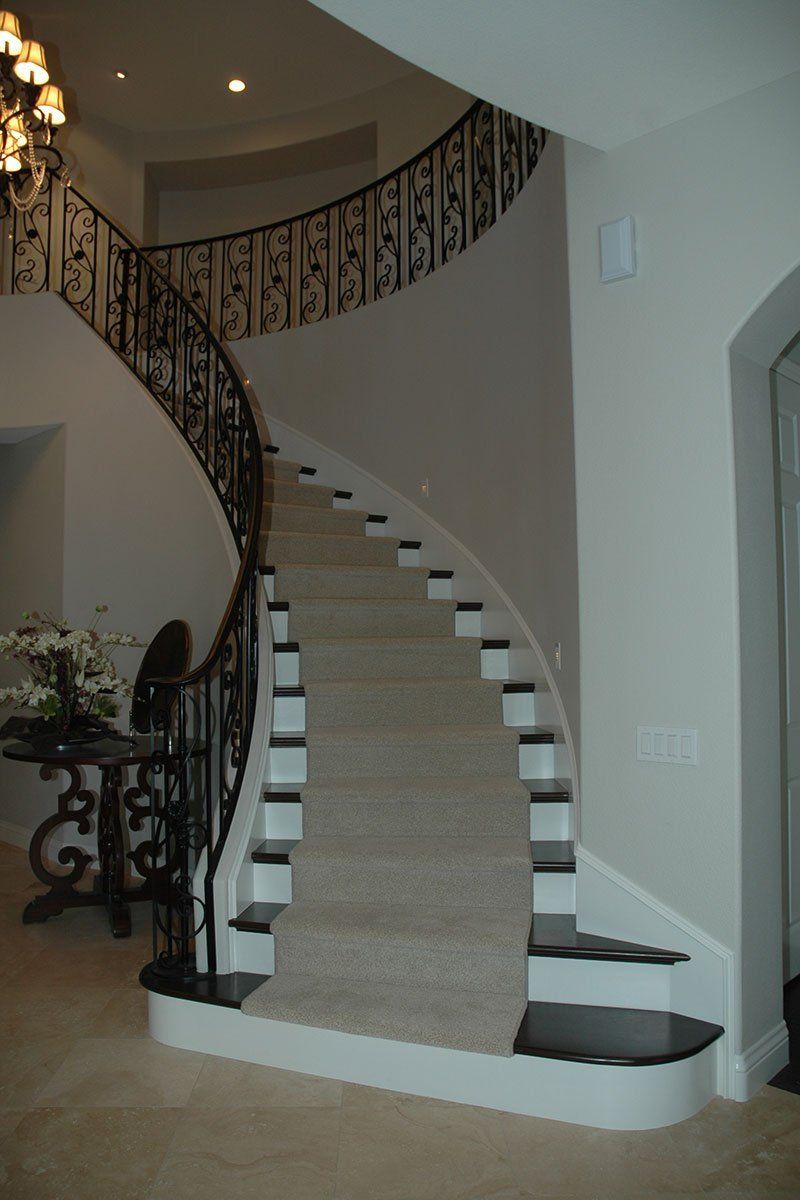Curved staircase with beige carpet, dark wrought-iron railing, and a chandelier in a home foyer
