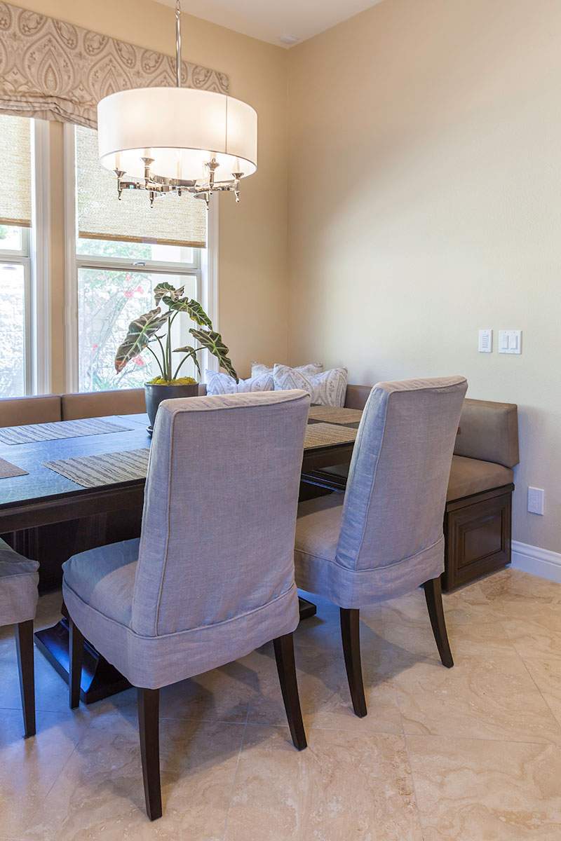 Dining room with upholstered chairs around a wooden table, a window, and a pendant light, in neutral tones