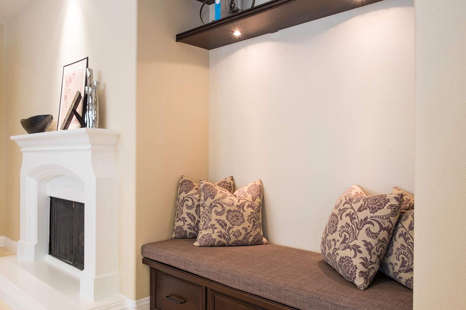 Bright living room corner with a white fireplace and a built-in bench with patterned cushions and pillows.