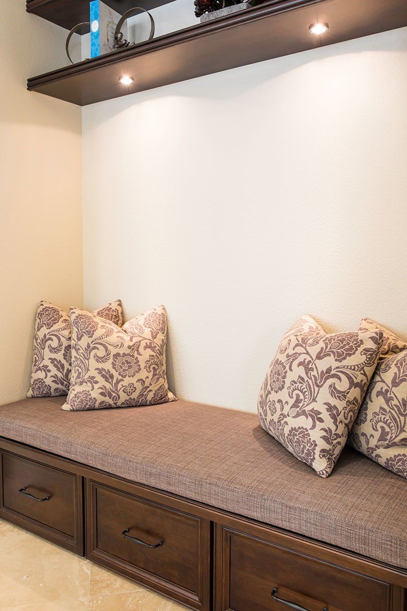 Built-in window seat with beige cushion, patterned pillows, and dark wood storage drawers under shelves