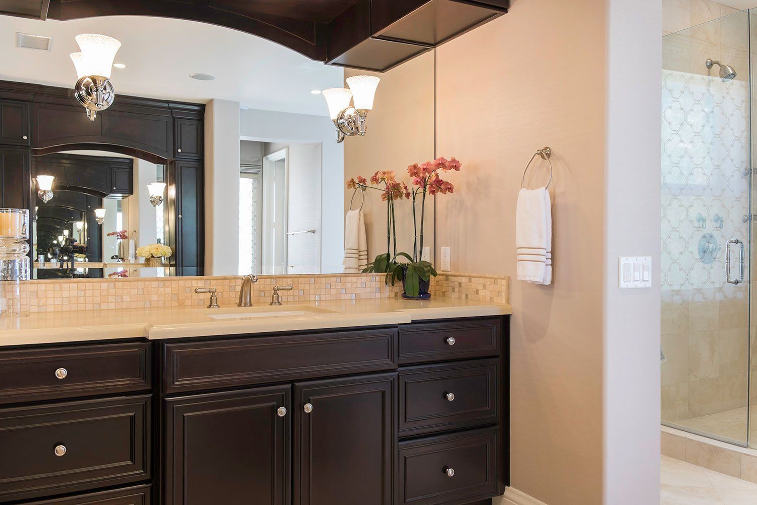 Bathroom vanity with dark wood cabinets, beige countertop, mirror, and orchid decor