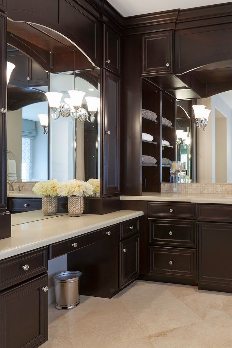 Elegant bathroom vanity with dark wood cabinets, large mirrors, and white countertops.