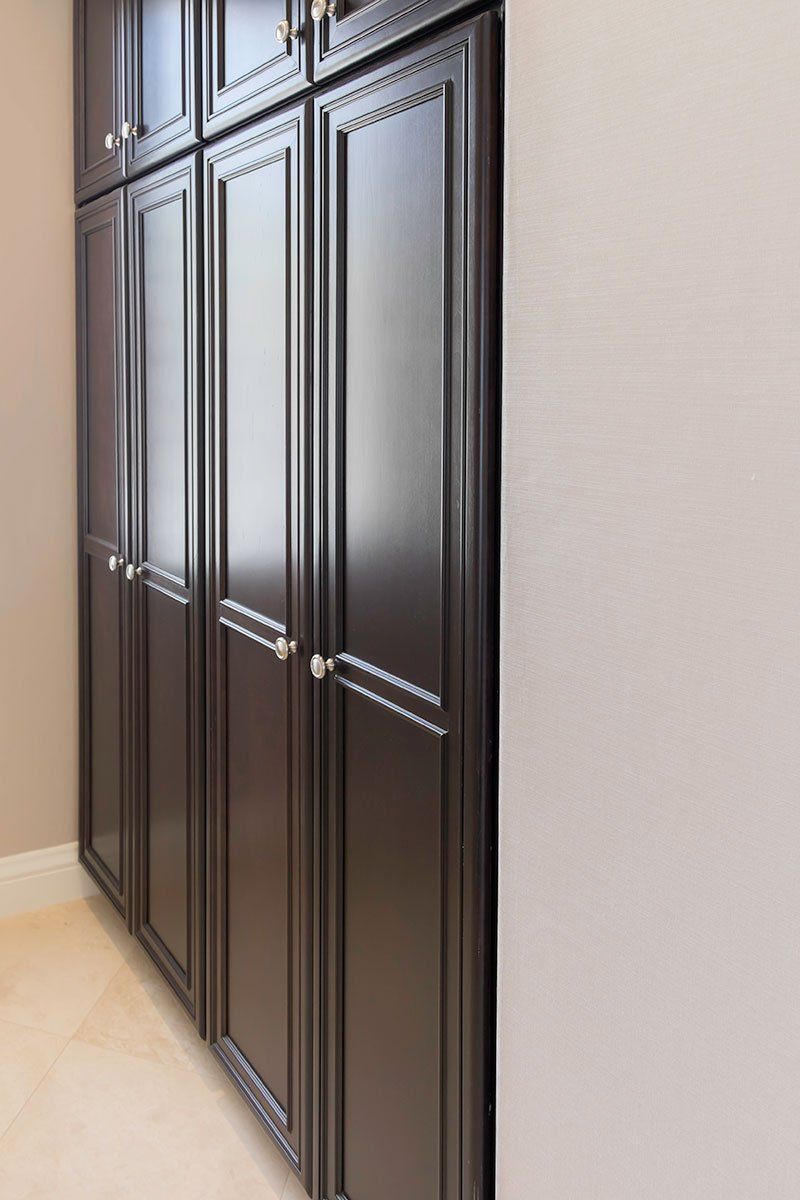 Dark wood built-in wardrobe cabinets along a beige wall in a hallway.