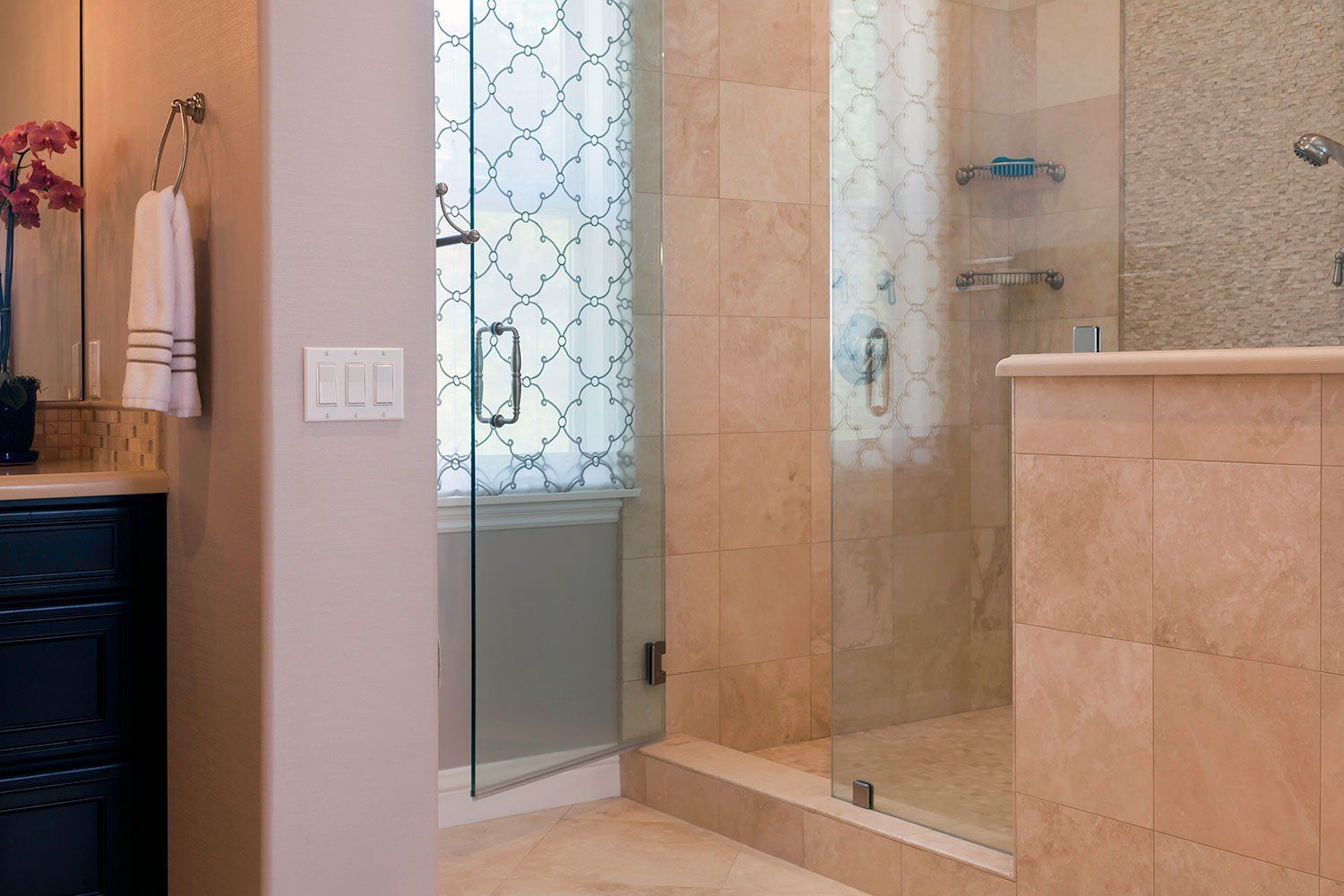Bathroom with glass shower, tiled walls, and a vanity with towels on the left.