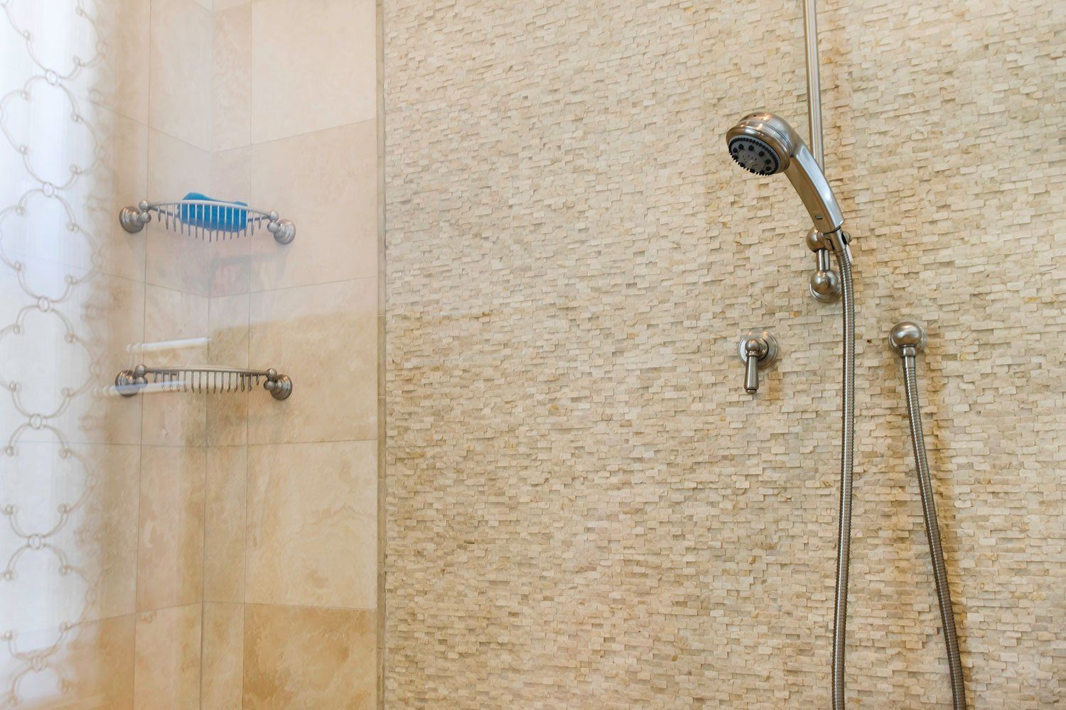 Shower with handheld and fixed showerheads on a beige tiled wall