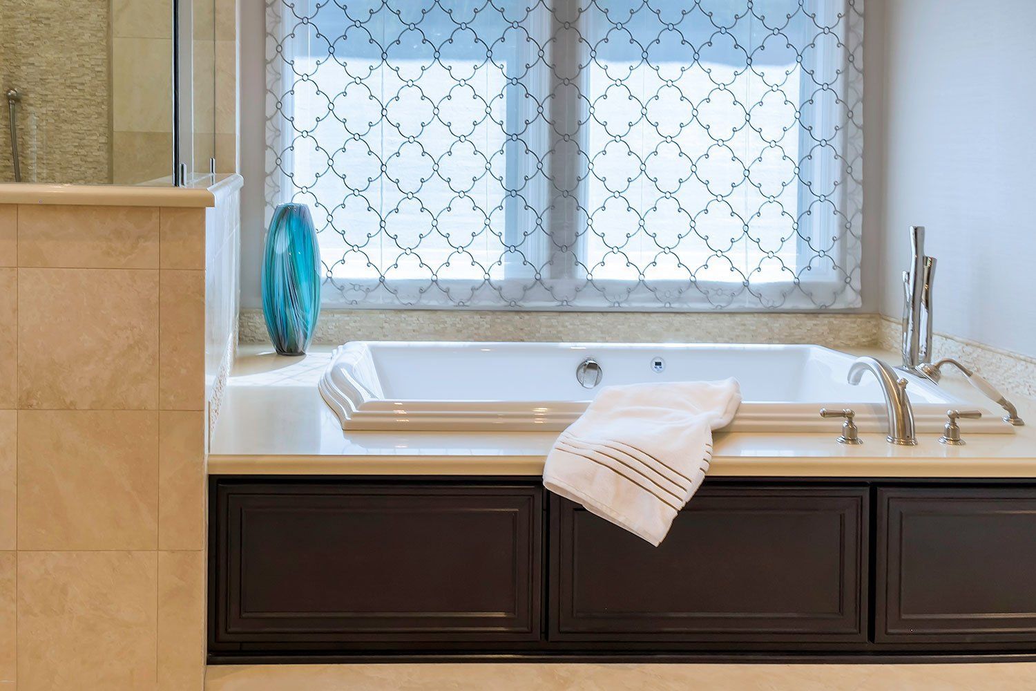 Bathroom with a white tub, dark cabinets, a folded towel, and a window with patterned glass curtain