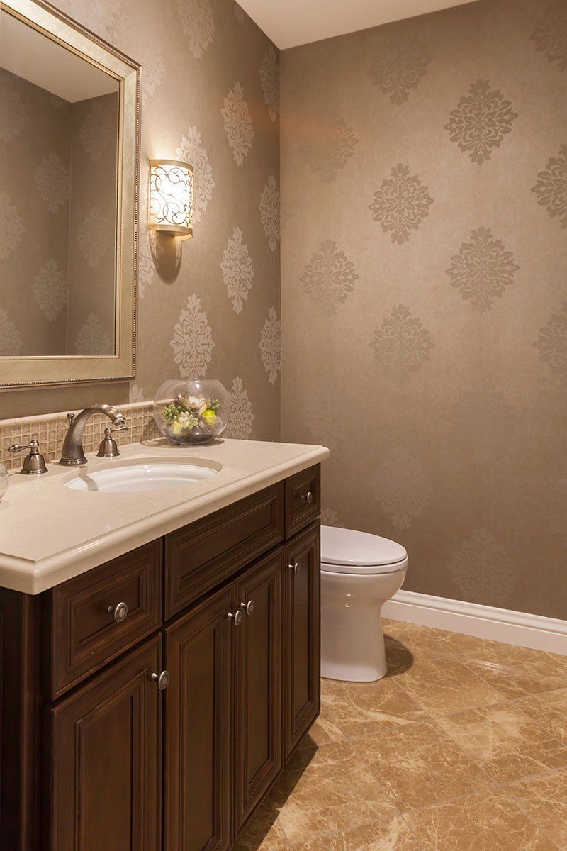 Small bathroom with dark wood vanity, white sink, mirror, wall sconce, and toilet on beige carpet.