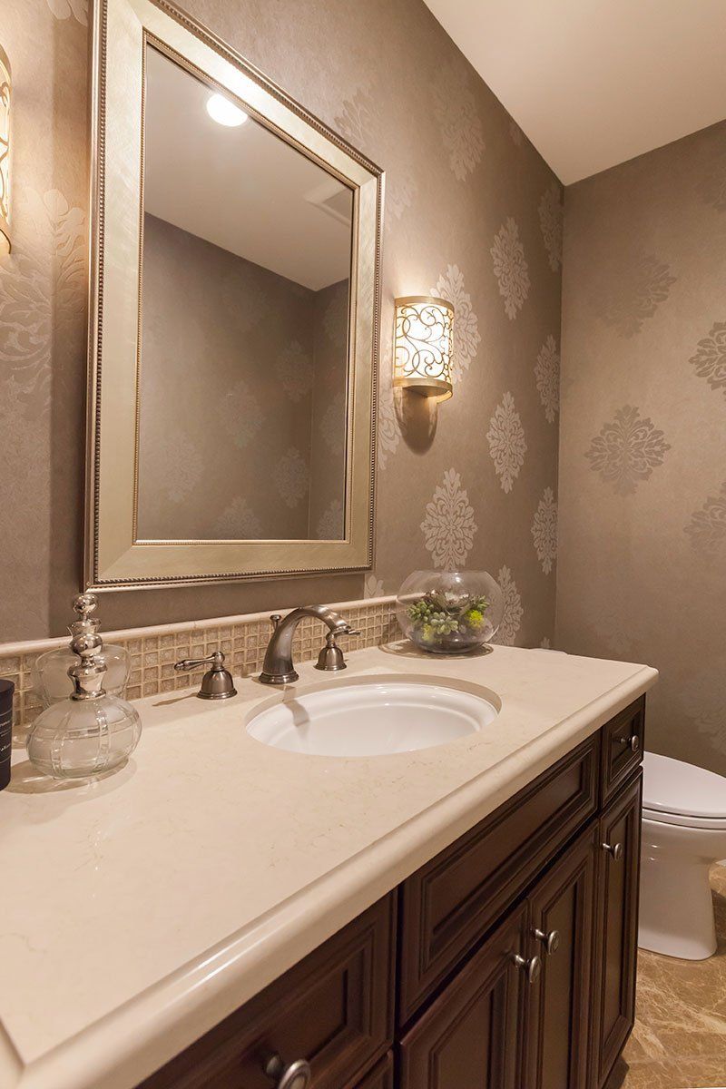 Elegant bathroom vanity with mirror, white countertop, and dark wood cabinets under warm wall sconces