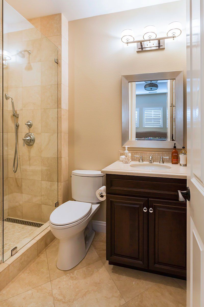 Small bathroom with glass shower, toilet, and dark wood vanity with mirror and lights.