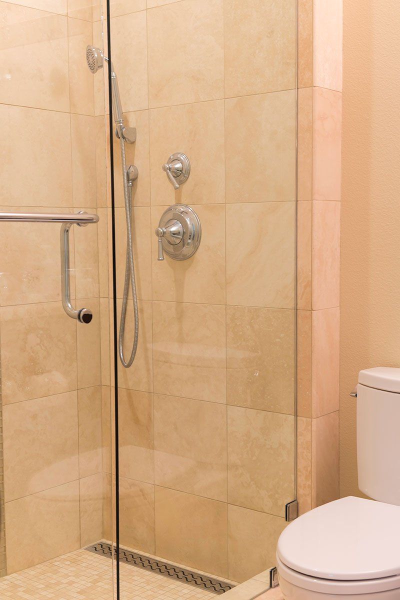 Beige-tiled bathroom with glass shower, chrome fixtures, and a toilet edge visible.