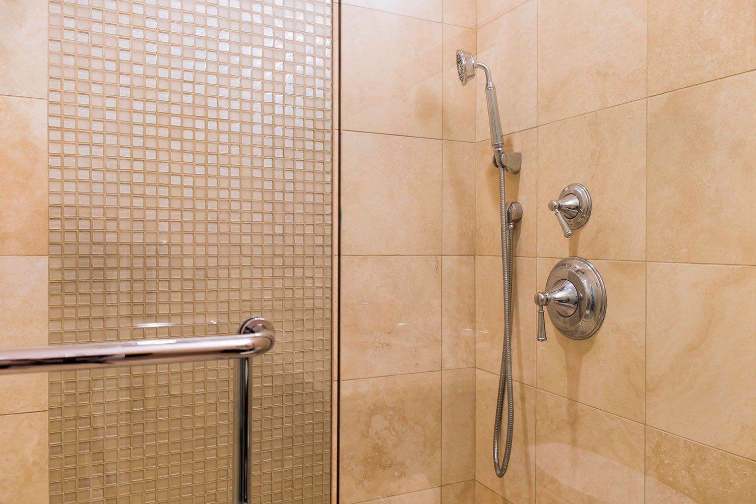 Tiled bathroom shower with handheld showerhead, controls, and glass partition panel