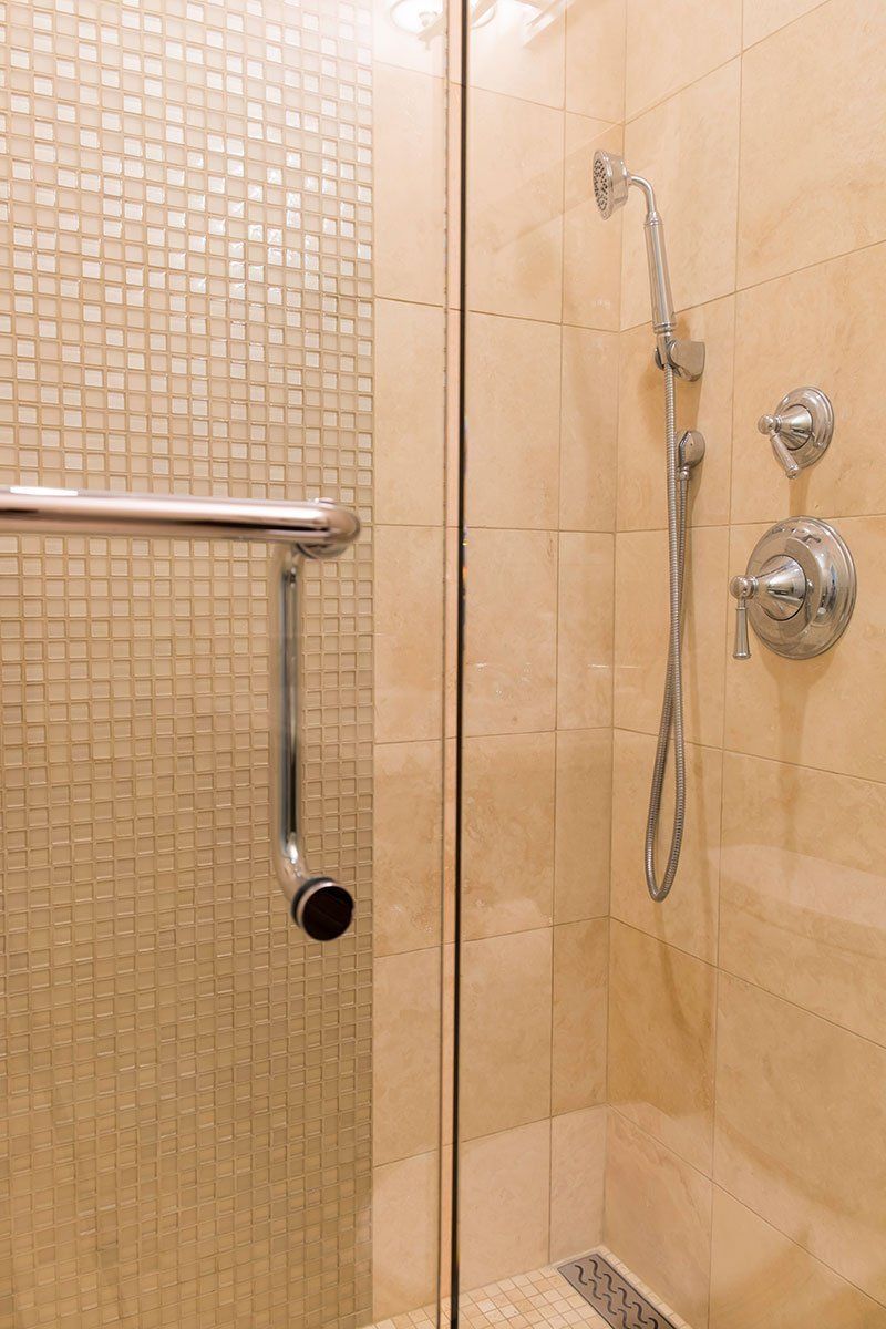 Tiled shower stall with chrome grab bar, handheld showerhead, and wall-mounted controls