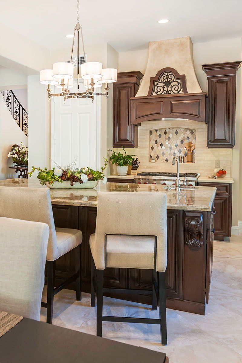Bright kitchen with island seating, chandelier, white cabinets, and ornate range hood
