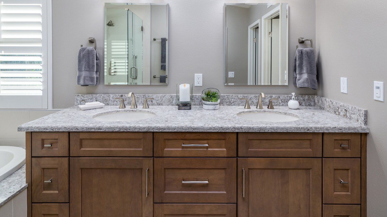 Bathroom vanity with granite countertop, double sinks, mirrors, and wooden cabinets