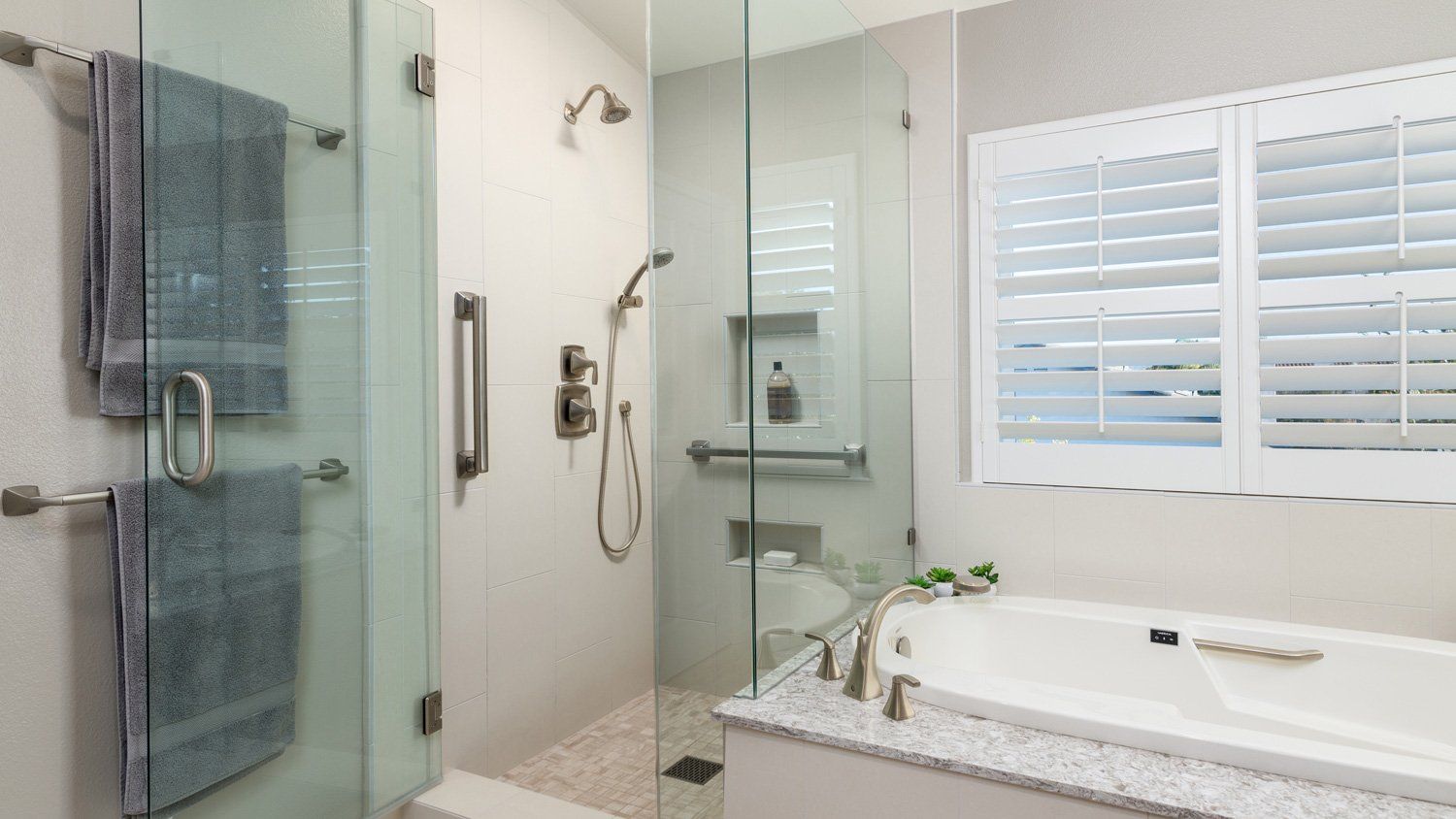 Modern bathroom with glass shower, white soaking tub, and towel rack near a window