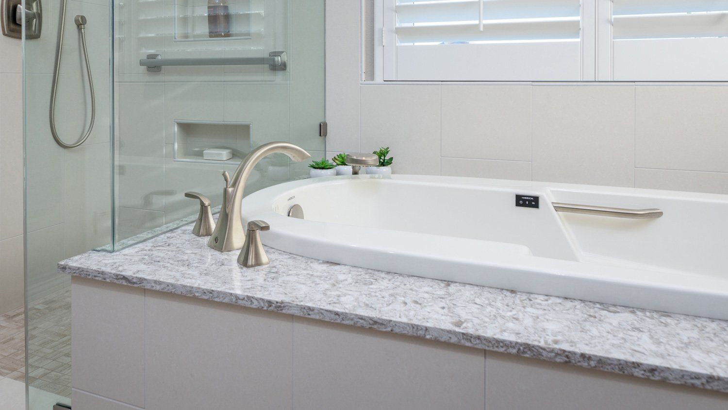 Bright modern bathroom with a white soaking tub, granite countertop, and glass shower enclosure.