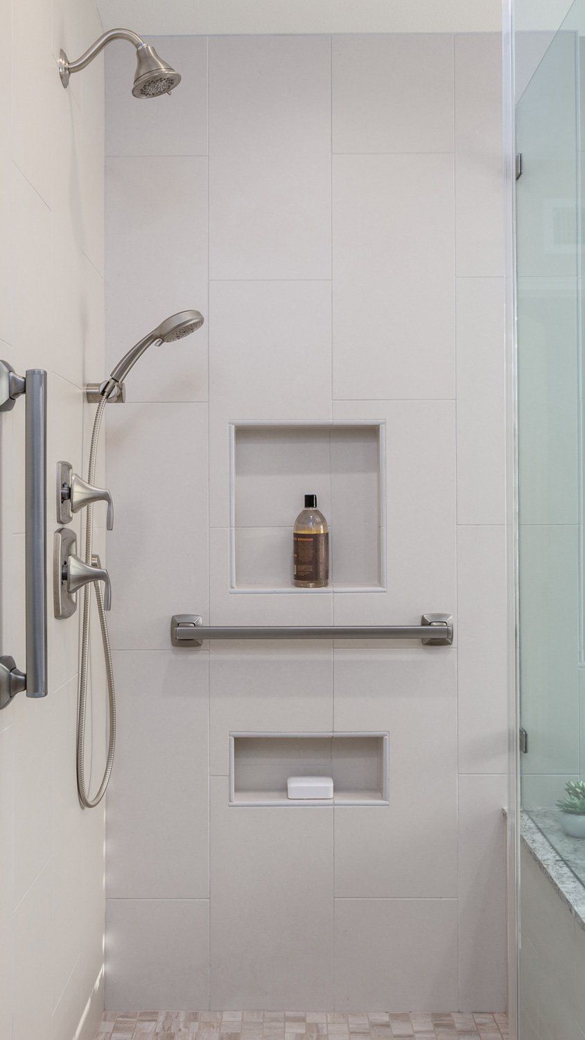 Modern white shower with chrome fixtures, built-in niches, and glass enclosure panel