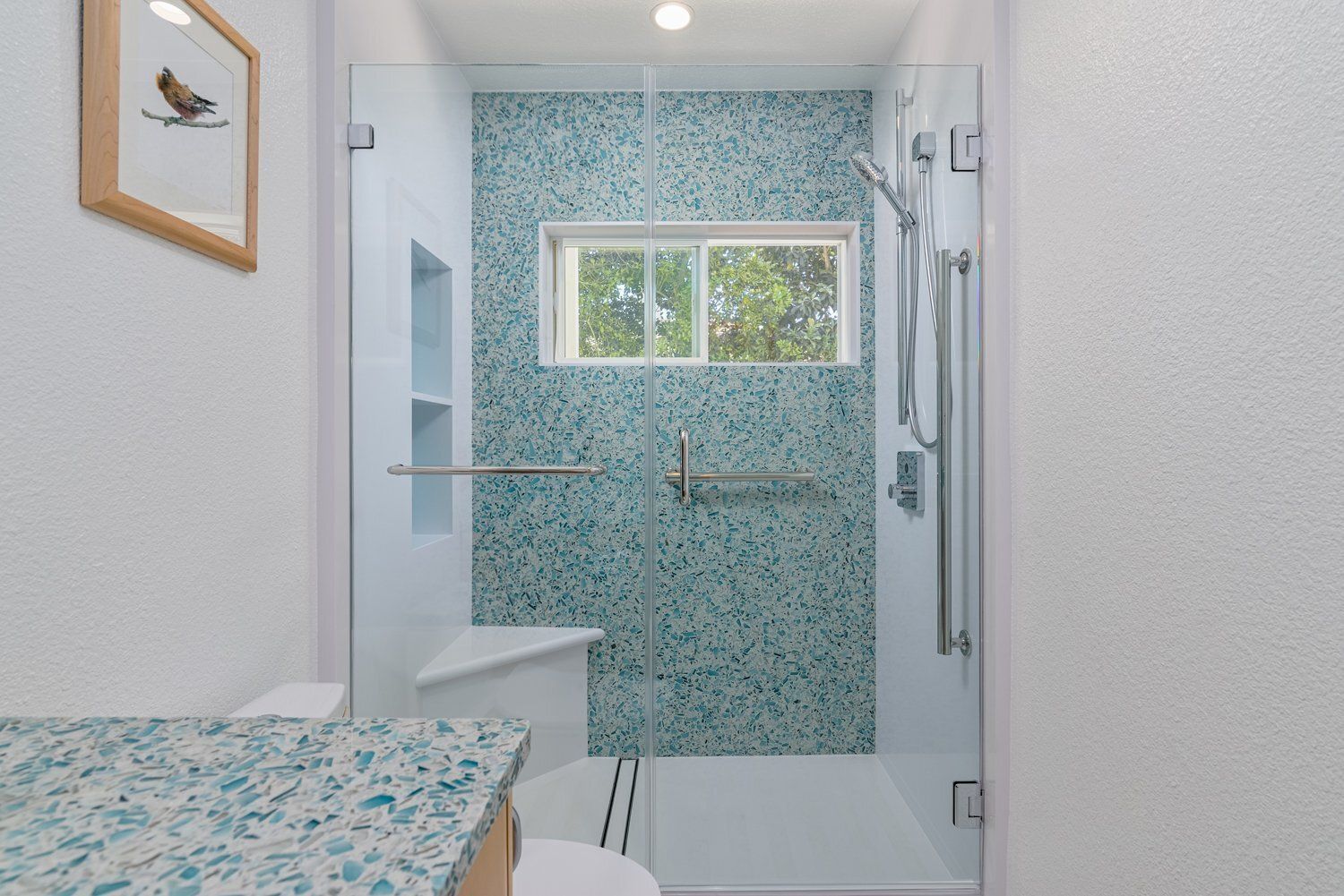 Bright bathroom with glass shower, white tile, and blue mosaic accent wall with window.