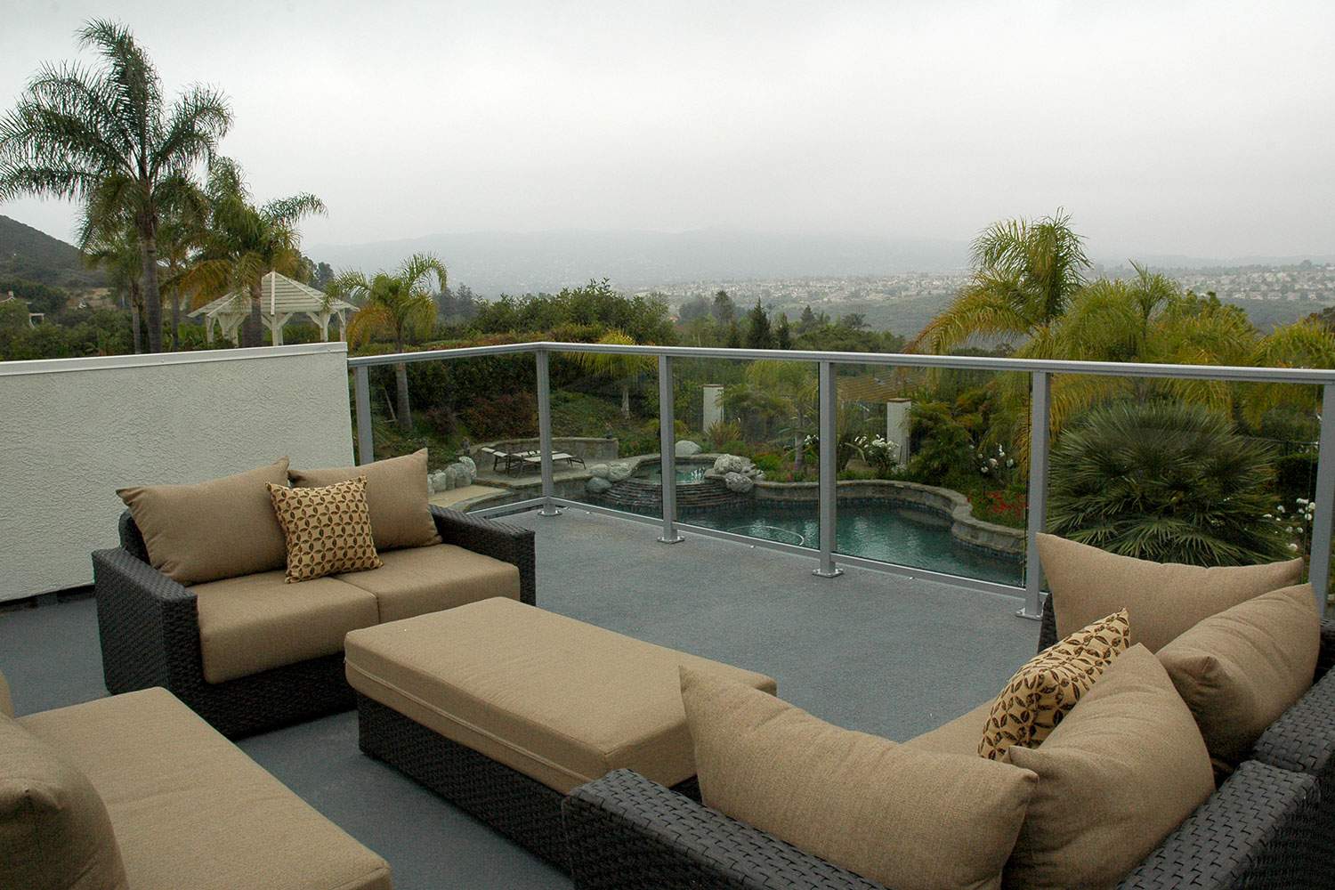 Outdoor patio with tan sectional seating and glass railing overlooking a hazy city and hills