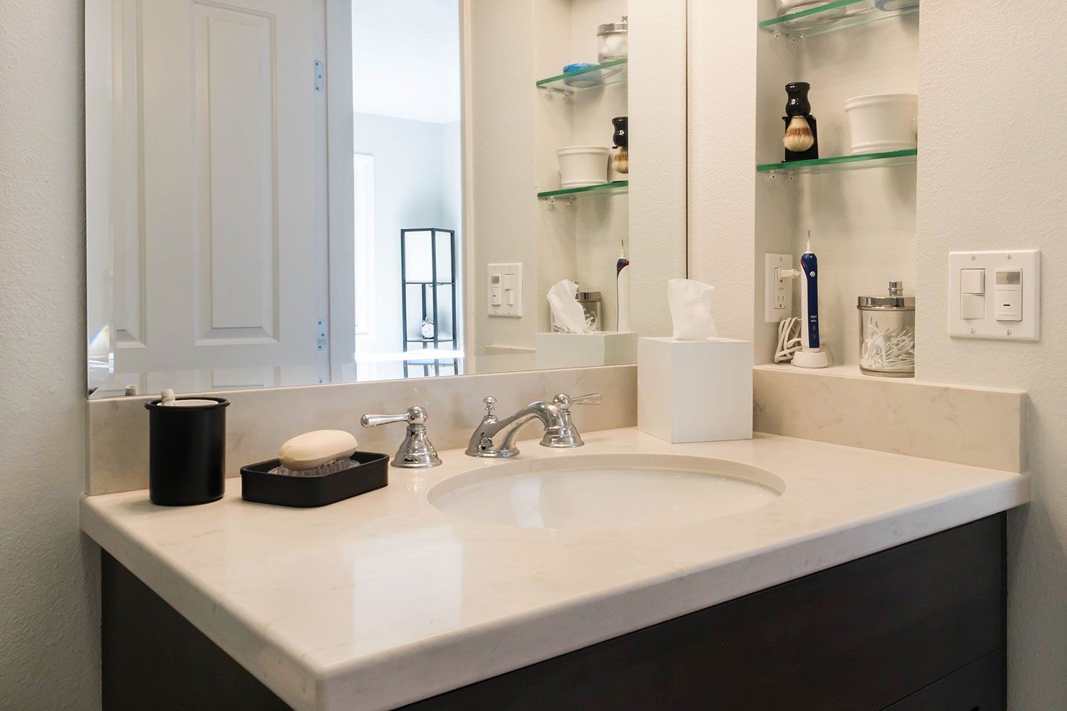 Bright bathroom vanity with white sink, mirror, shelves, and toiletries