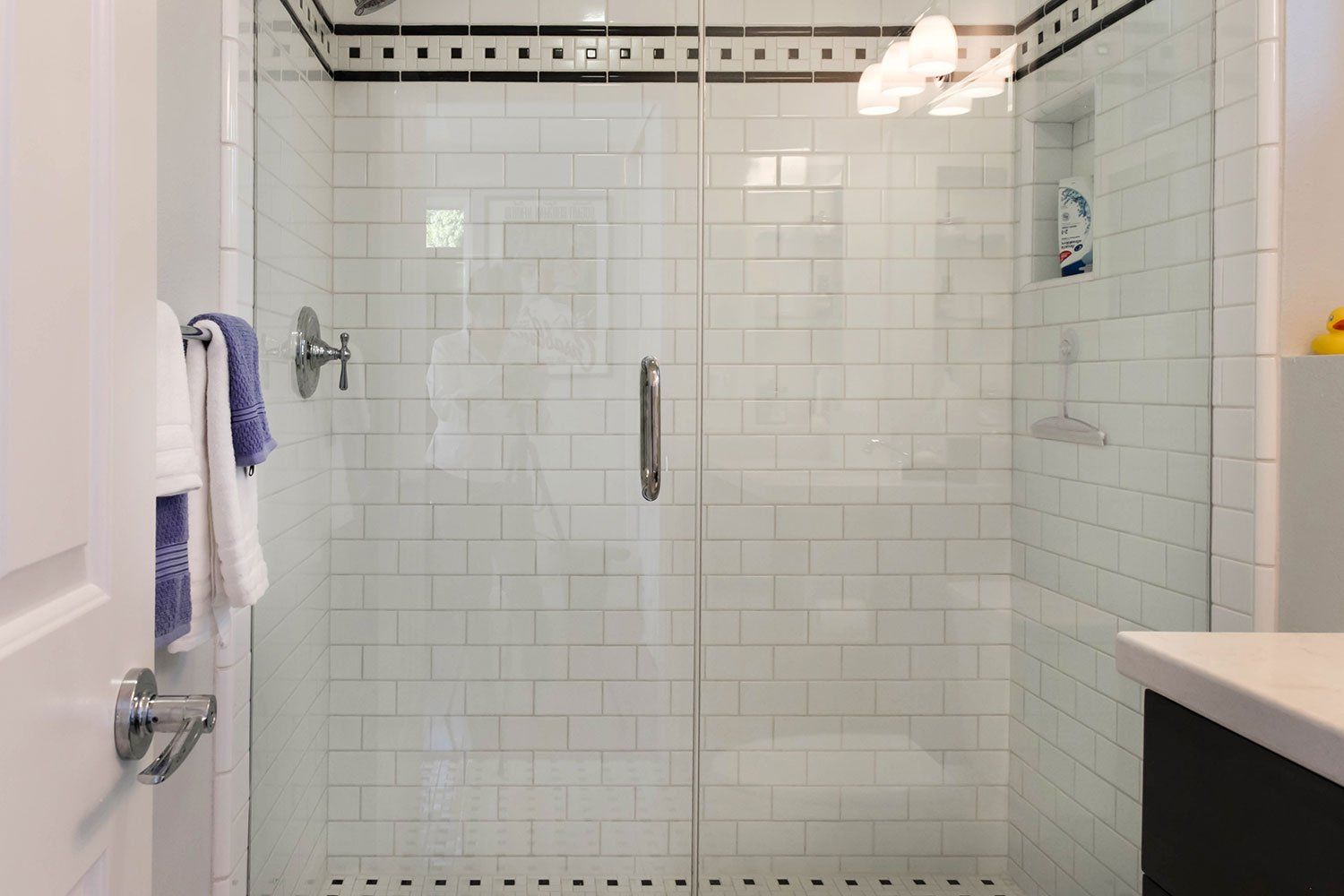 Tiled glass shower enclosure with chrome fixtures in a white bathroom