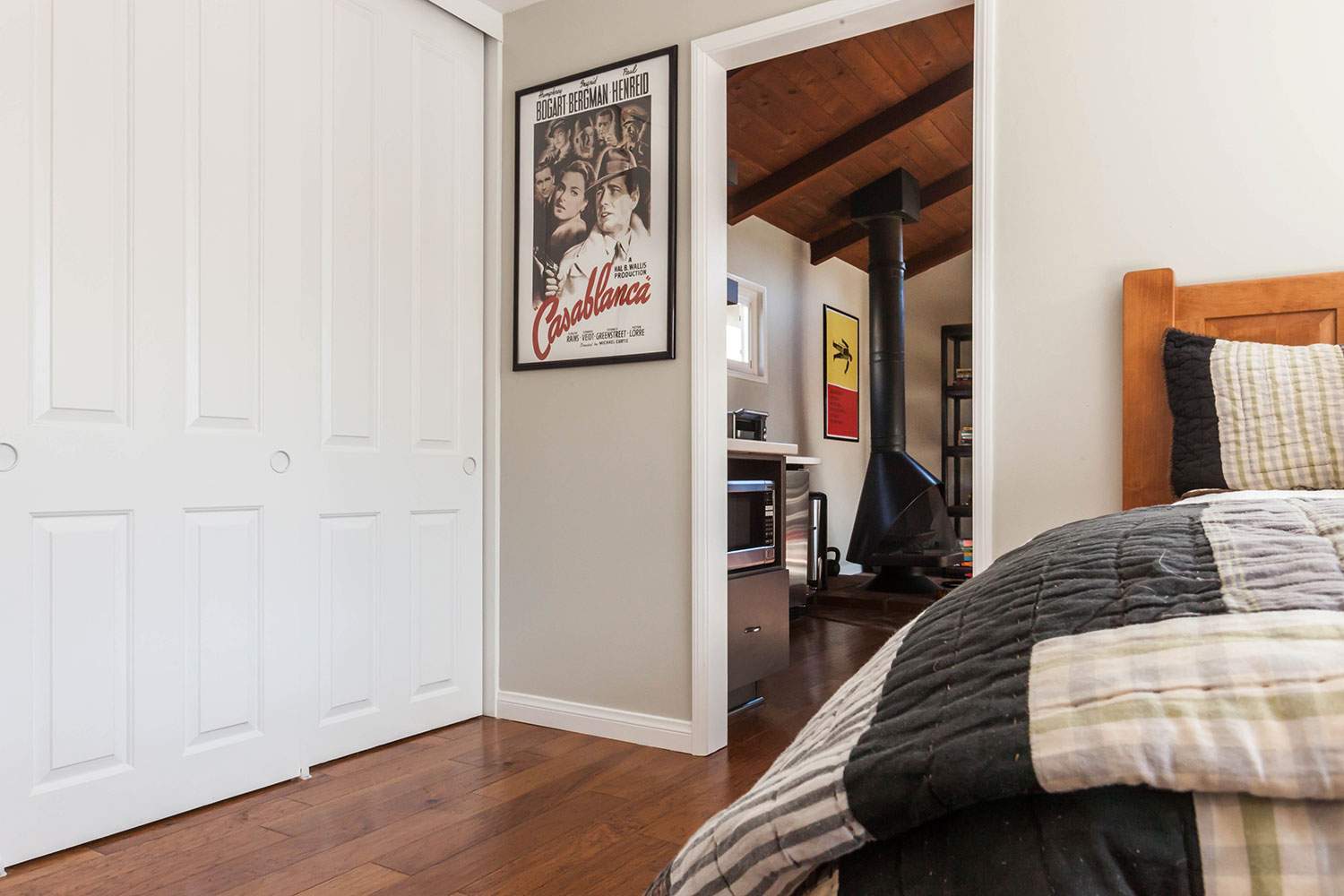 Cozy bedroom with white closet doors, wooden floor, framed wall art, and an open doorway to another room