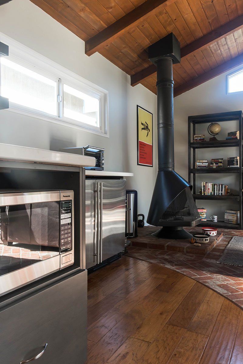 Modern living room with wood ceiling, black wood stove, fireplace, and shelving on hardwood floors