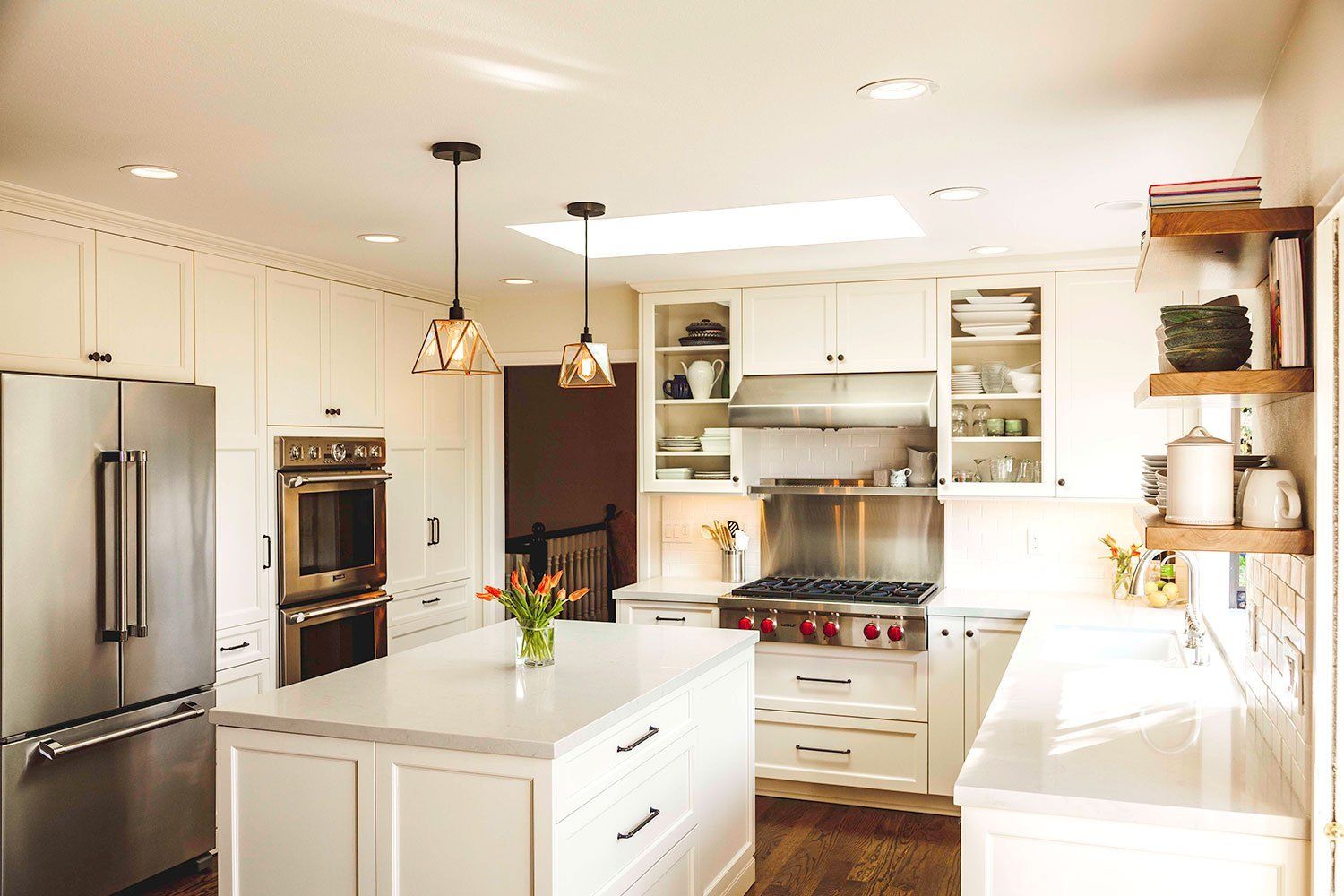 Bright white kitchen with island, stainless steel fridge, double oven, and sunlit cabinets