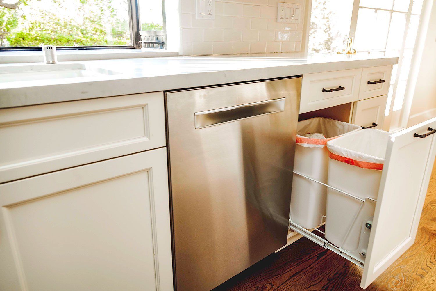 Kitchen with stainless dishwasher and pull-out trash bins under a white countertop