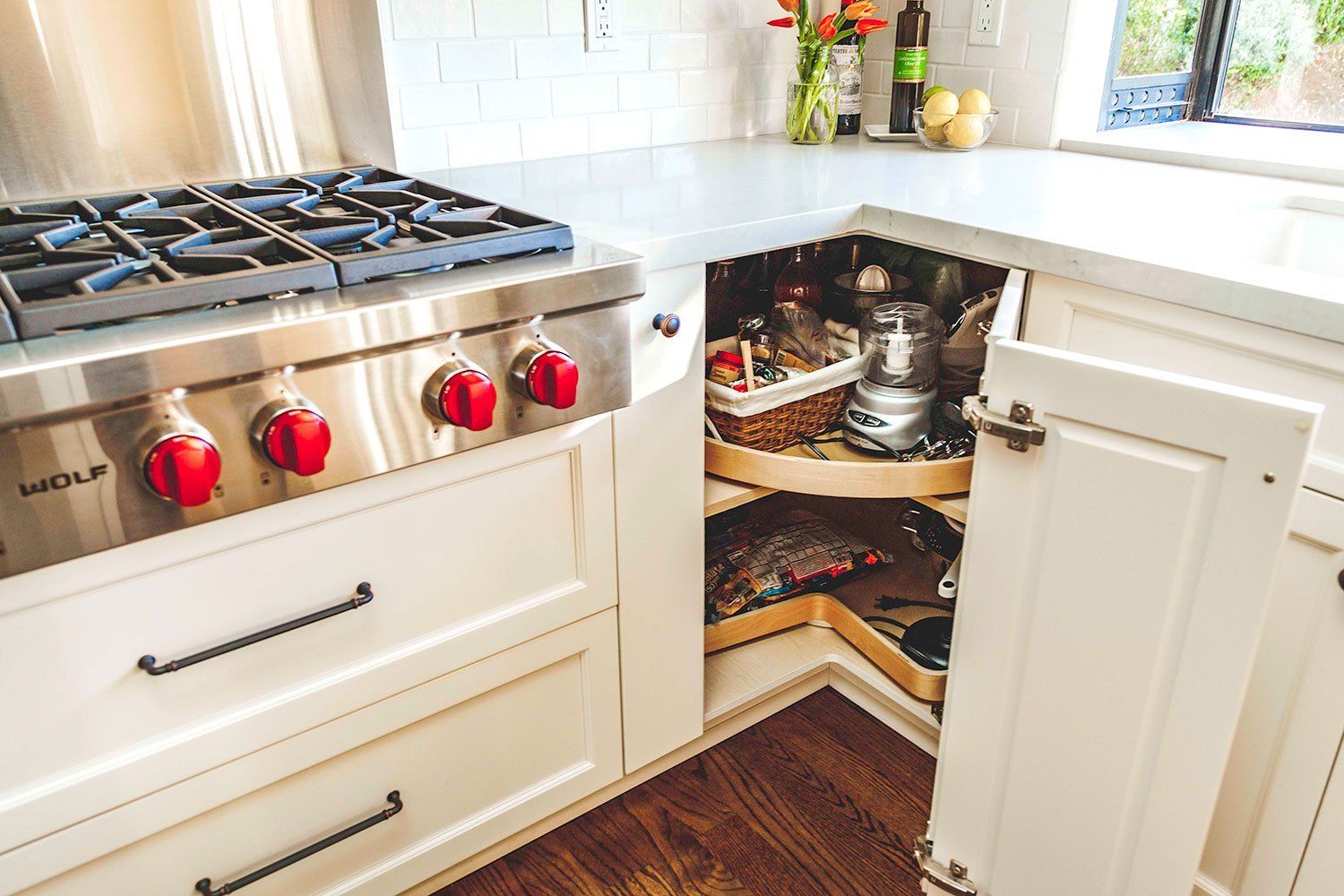 White kitchen with gas stove and open under-sink cabinet exposing plumbing and storage clutter