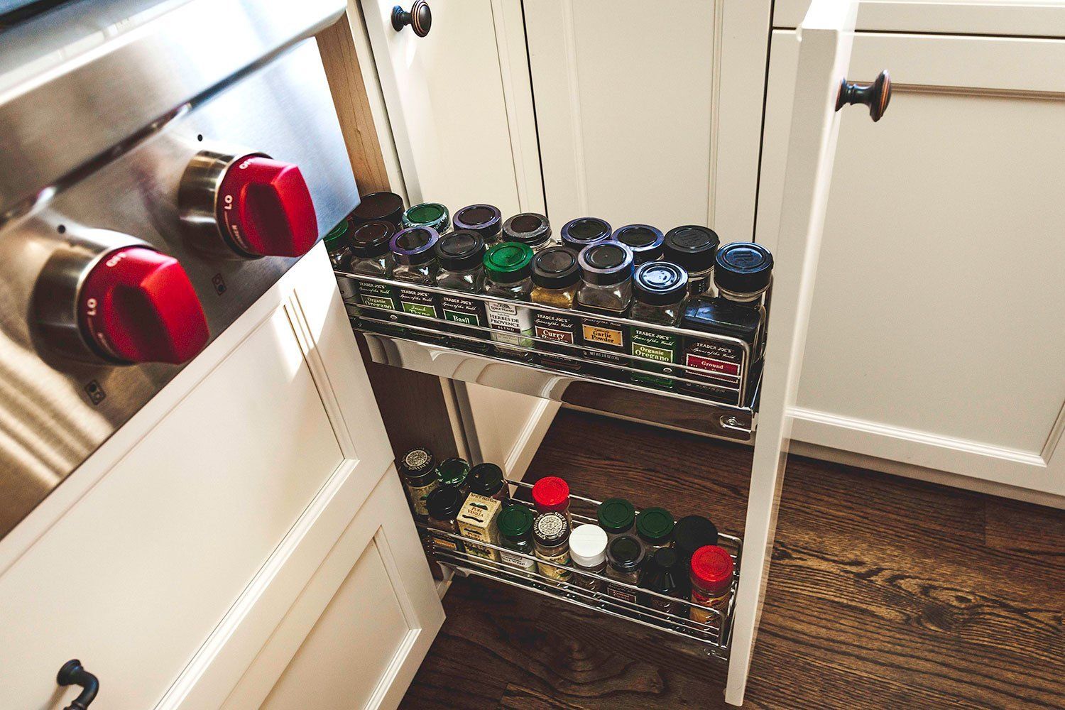 Spice jars on a small metal rack in a kitchen cabinet, with red-lidded containers nearby.