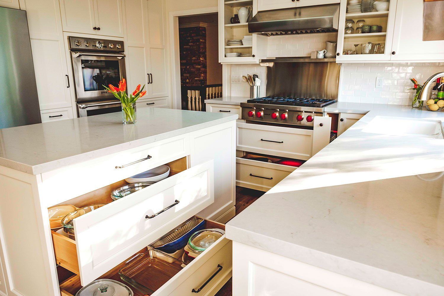 Bright modern kitchen with white island, open drawer, and stainless steel stove with built-in ovens.