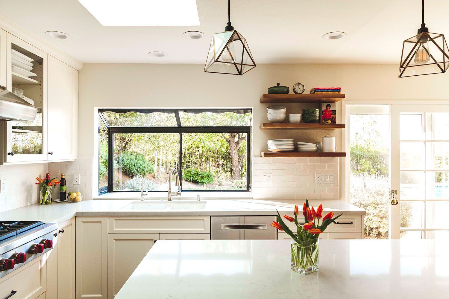 Bright modern kitchen with white cabinets, open shelves, large windows, and flowers on the island.