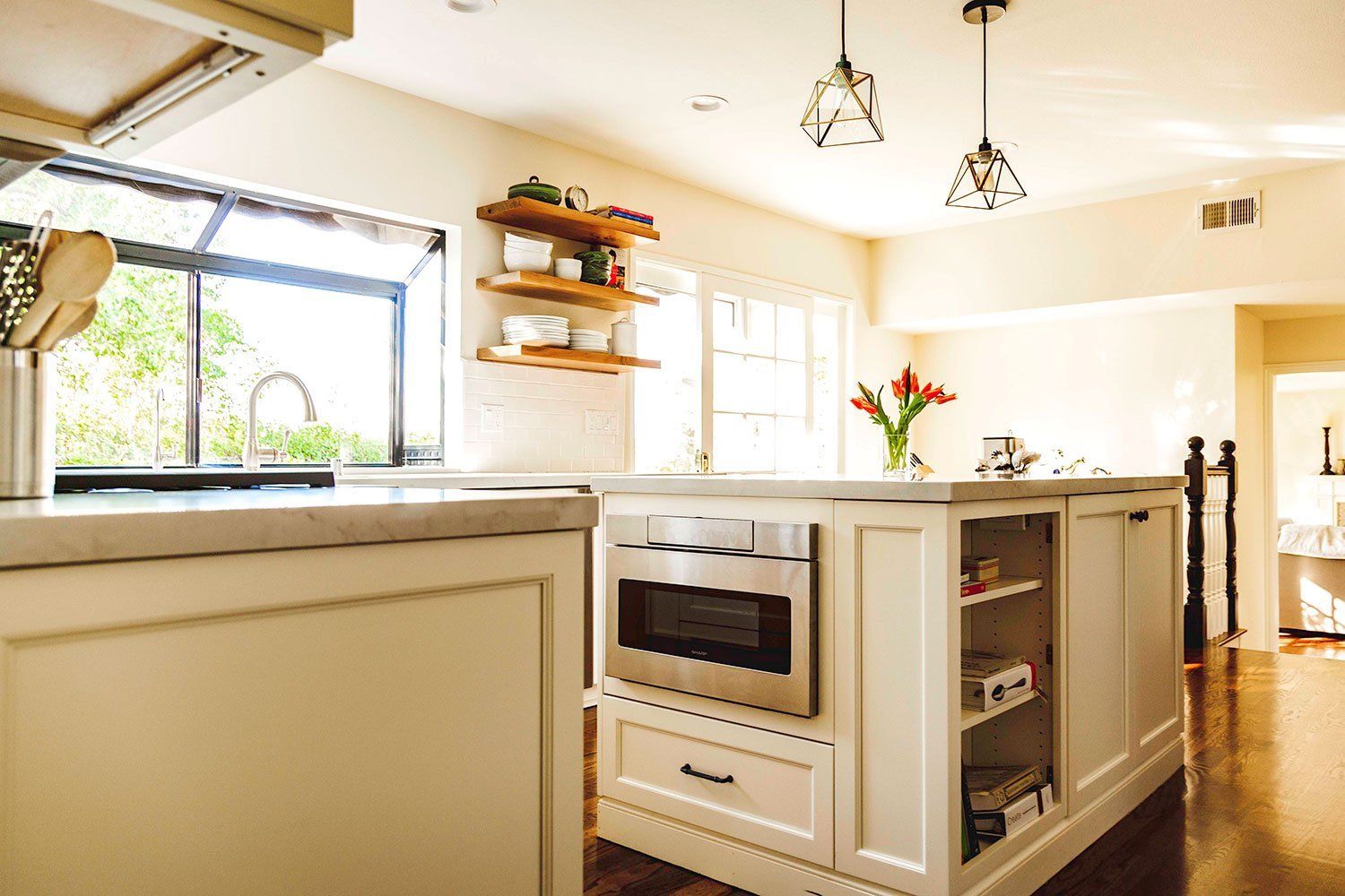 Bright modern kitchen with white cabinets, island, and large window overlooking greenery