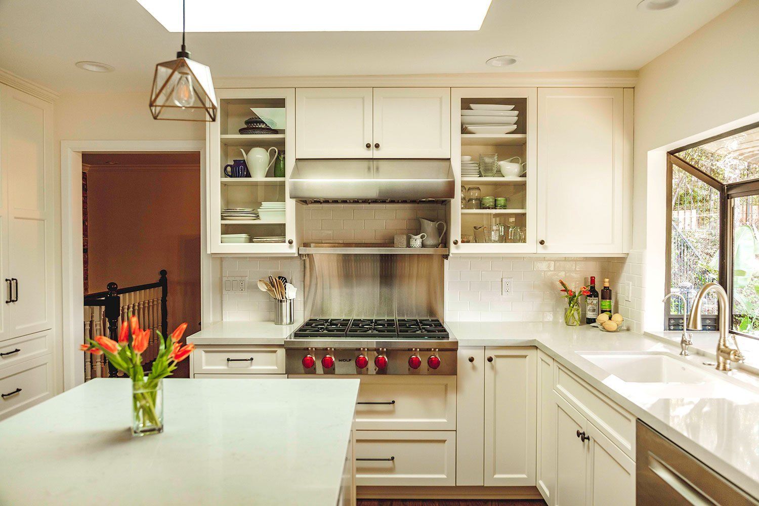 Bright modern kitchen with white cabinets, stainless stove, and a vase of orange flowers on the island