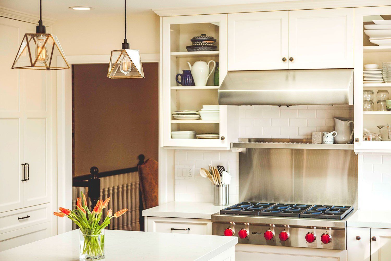 Bright white kitchen with pendant lights, island, and stainless steel stove under open shelves