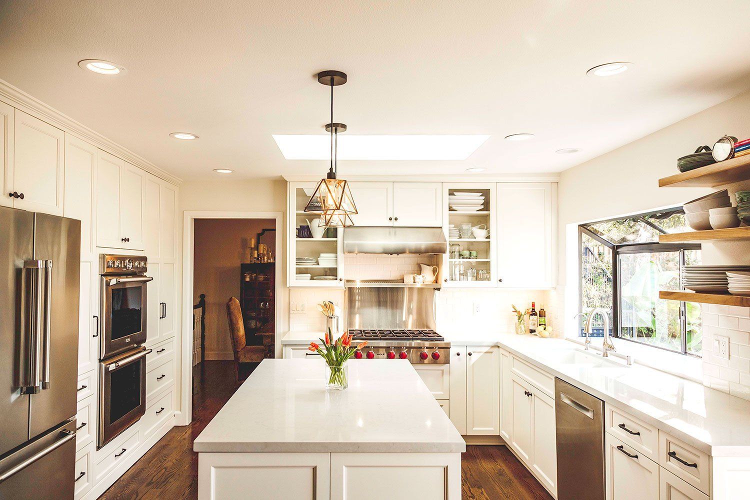 Bright modern kitchen with white cabinets, stainless steel fridge, island, and pendant light fixture