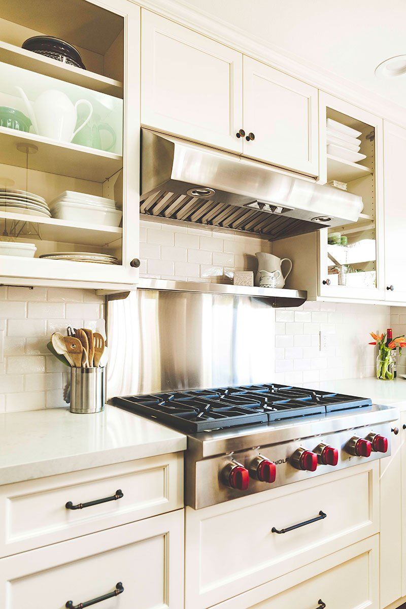 Bright white kitchen with a gas range, stainless steel hood, and open shelves with dishes