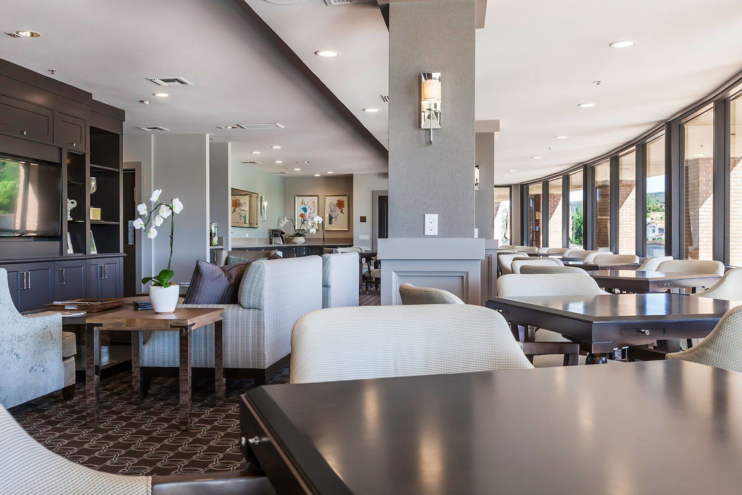 Modern restaurant lounge with gray seating, tables, and large windows overlooking the water