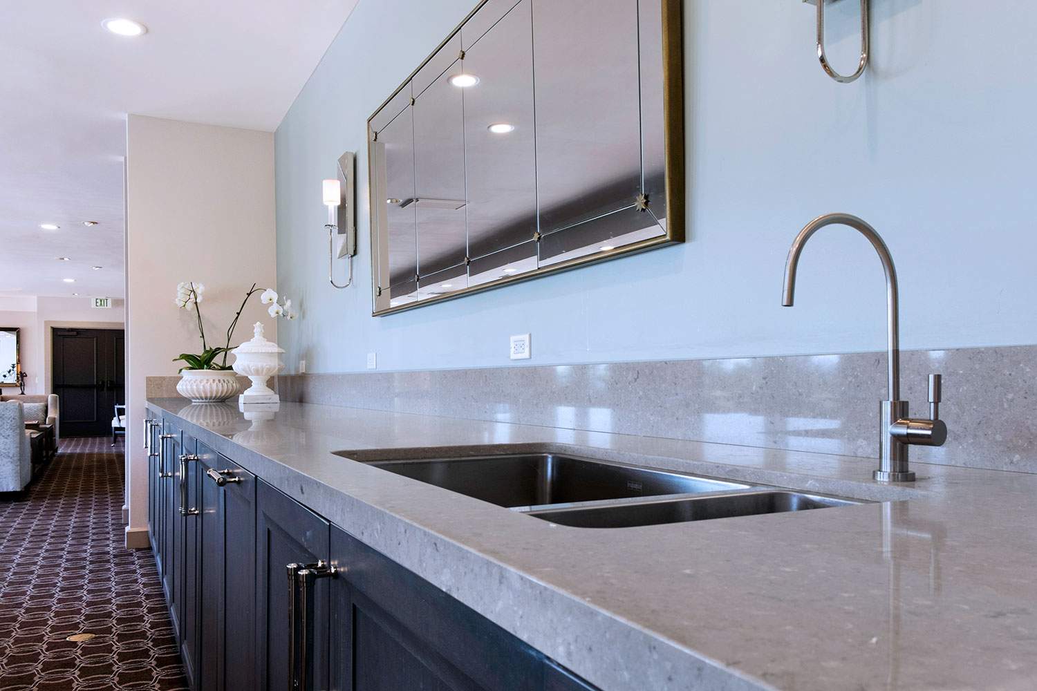 Modern kitchen with long granite countertop, sink, faucet, and large wall mirror.