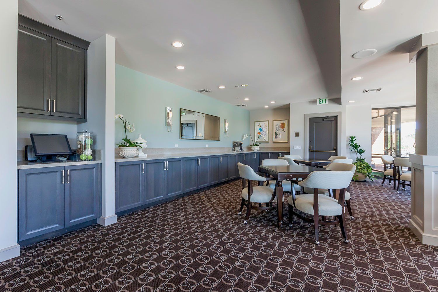 Spacious modern dining area with blue cabinets, round table, and patterned carpet under recessed lights