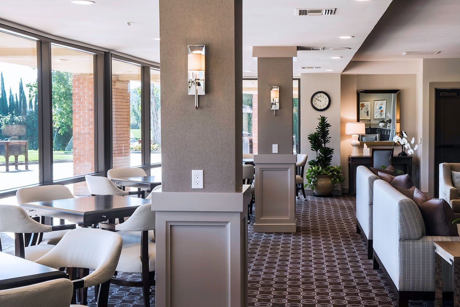 Modern hotel lounge with tables, chairs, sofas, and a patterned carpet by large windows